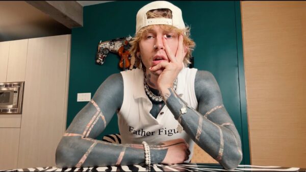 mgk leans against his hand while looking at the camera, in a scene from the new music video no cell phones in rehab.