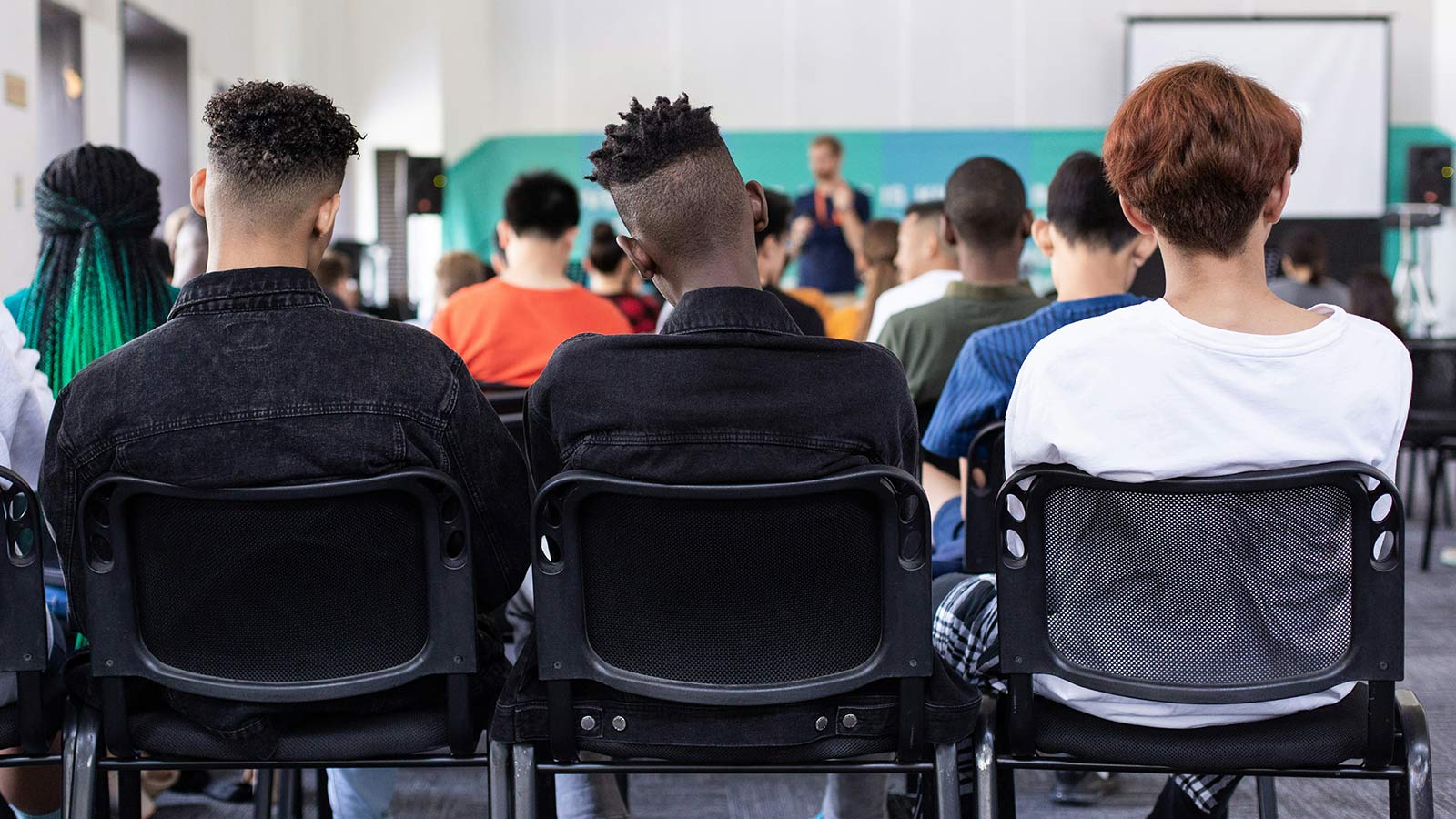 The backs of three students at a school assembly.
