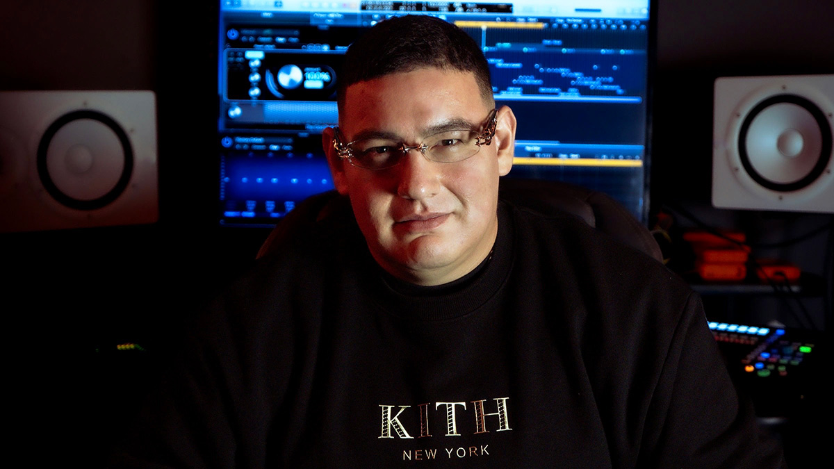 Producer MoeZart Beats poses for a photo while sitting in front of equipment in a recording studio.