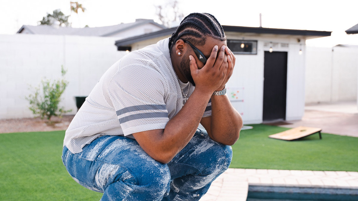 Recording artist Shea Smilez crouches while holding his head in his hands