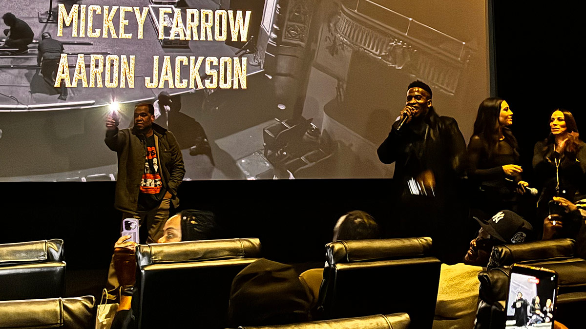 Godfrey stands at the front of a theatre, addressing the audience, at the screening for his new comedy special, Rebel with a Cause.