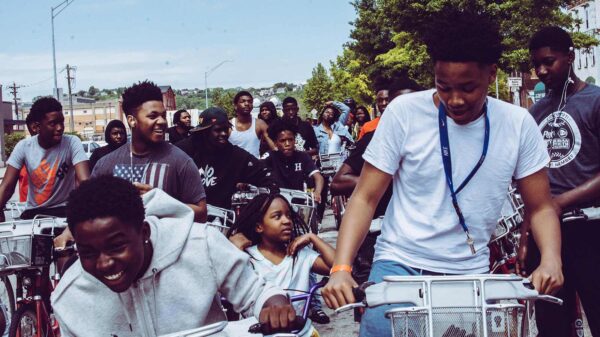 Children riding bicycles in a group on a city street, used to illustrate articles about the 6-7 meme and the shared play culture of kids.