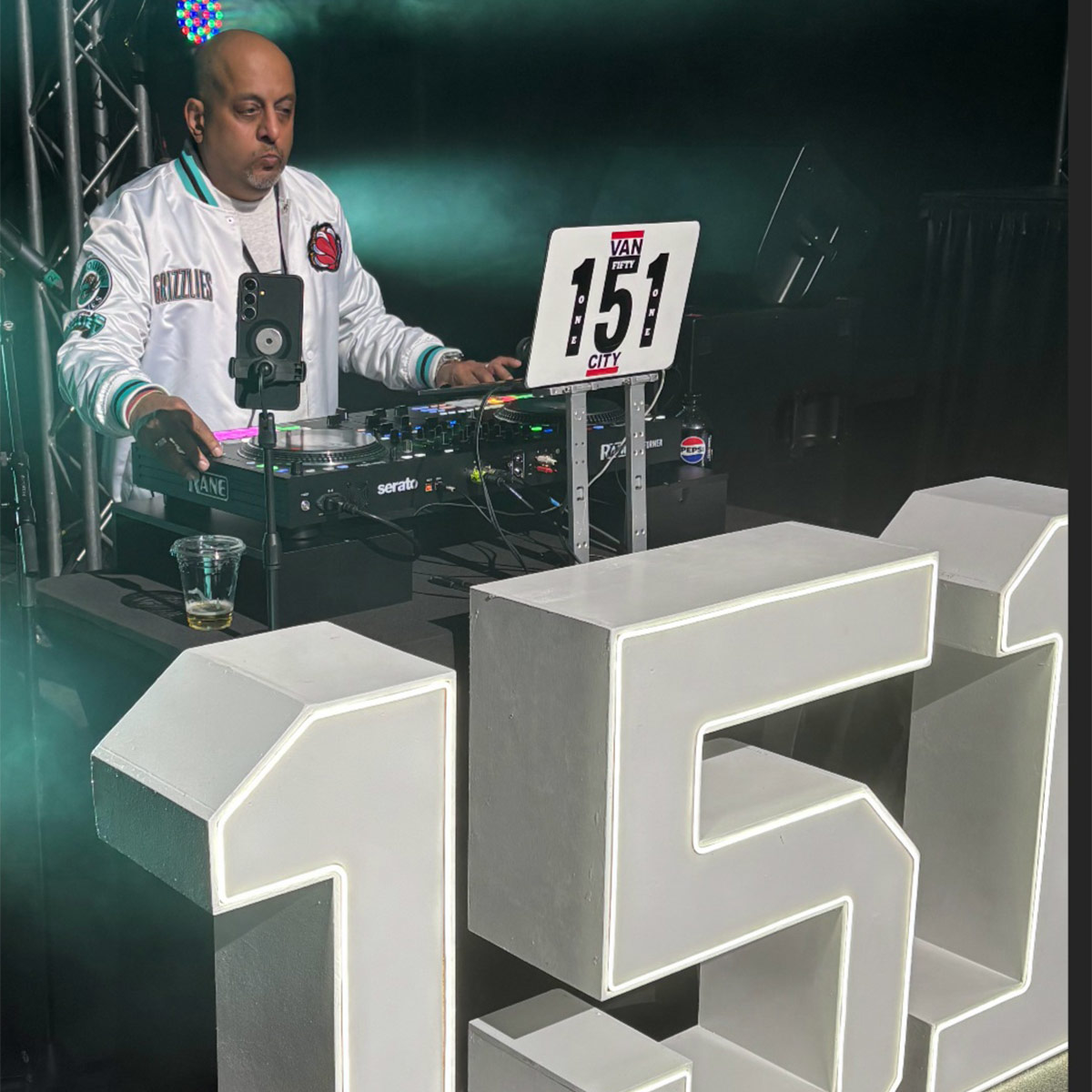 A DJ performs during an event with a large 151 sign in front of him.