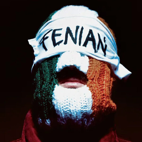 Kneecap member wearing a knitted tricolour, Irish-themed balaclava and a headband reading Fenian against a dark background.