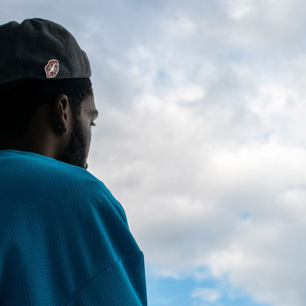 A young man wearing a baseball hat backwards looks up at the CN Tower in Toronto.