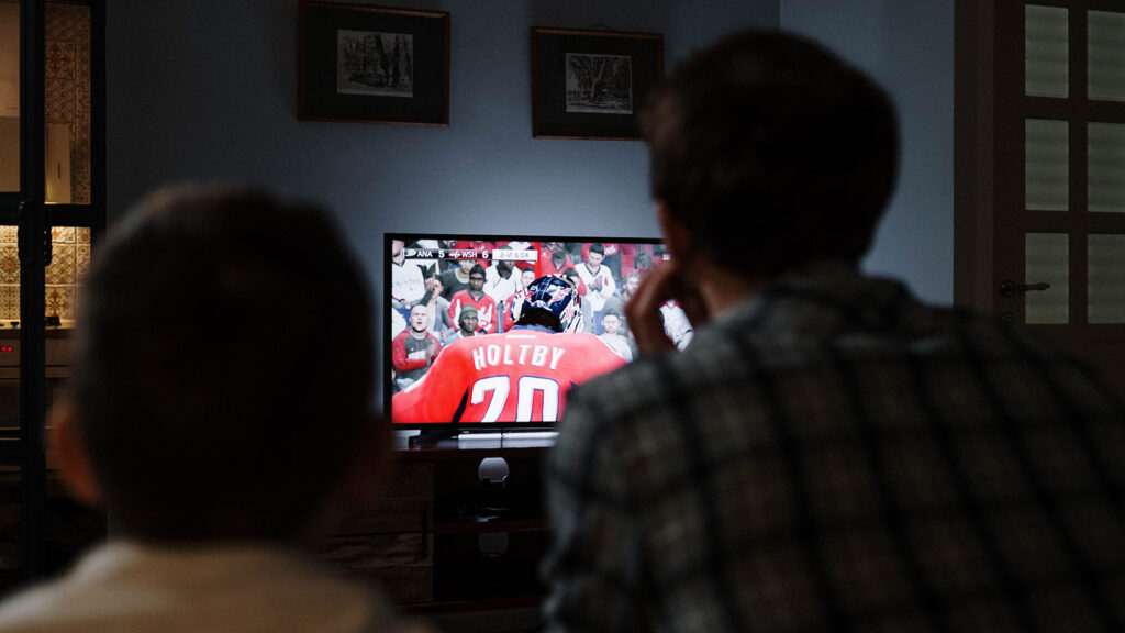 A from behind view of a father and son watching hockey on CBC.