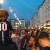 A young boy wearing a soccer jersey sits on an adults shoulders during a World Cup celebration outdoors.