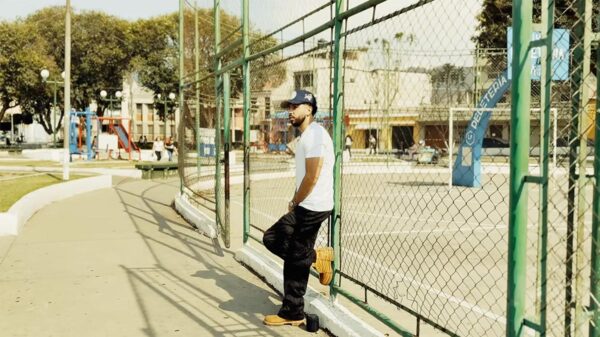 Romeo Don't Die leans against a fence in the Don't Die, I'll Cry music video.