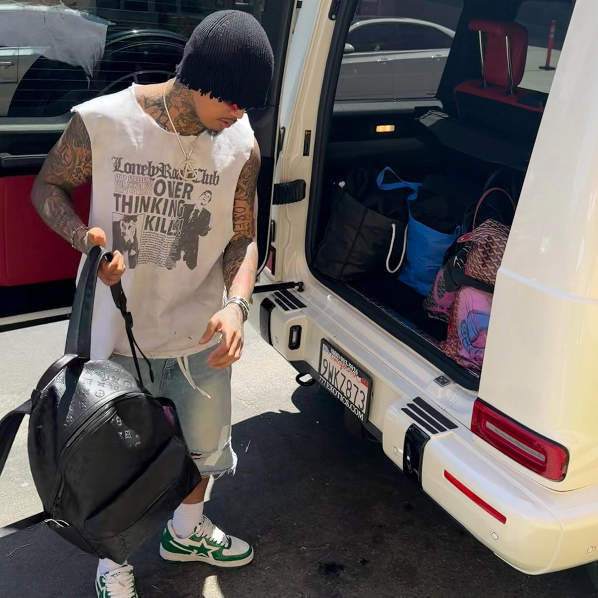 A man wearing a Lonely Road Club t-shirt loads a bag into a car.